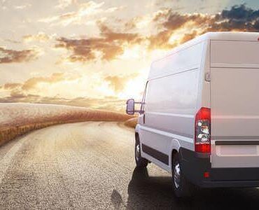 Weißer Transporter fährt bei Sonnenuntergang über eine Landstraße – Klaviere und Flügel