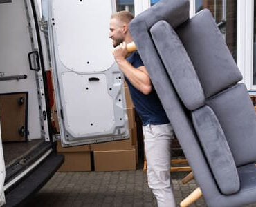 Möbellift Butzbach: Helfer tragen ein graues Sofa aus einem Transporter
