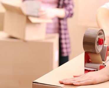 Verpackungsmaterial: Hand verklebt einen Umzugskarton mit Klebeband